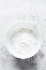 Fototapeta na wymiar Powdered sugar in a mixing bowl, measuring confectioners sugar for baking, a white mixing bowl with icing sugar