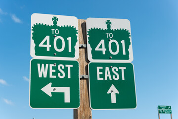 road signs in Toronto directing drivers to highway 401 with arrows pointing to west and east on a blue sky - obrazy, fototapety, plakaty