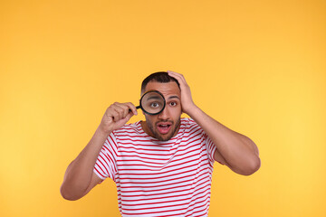 Shocked man looking through magnifier glass on orange background