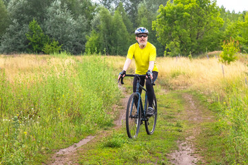 Fototapeta premium bearded man cyclist in yellow clothes rides a bike on a road in nature. sports, hobbies and entertainment for health