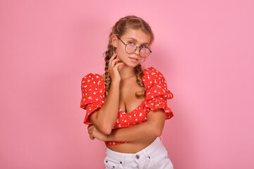 Young beautiful seductive Caucasian woman in glasses looks at screen and touches neck posing for modeling portfolio or student photo album stands on isolated pink background. Portrait of european girl