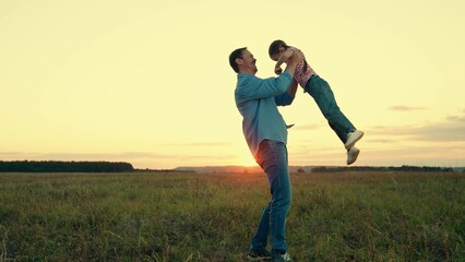 Smiling little daughter runs to hug loving father in country field at sunset - obrazy, fototapety, plakaty