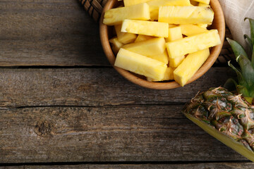 Pieces of tasty ripe pineapple in bowl on wooden table, flat lay. Space for text
