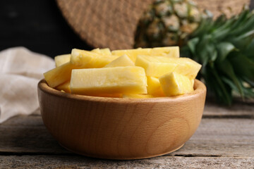 Pieces of tasty ripe pineapple in bowl on wooden table, closeup