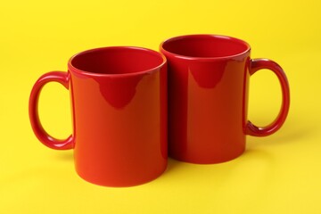 Two red ceramic mugs on yellow background