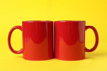 Two red ceramic mugs on yellow background