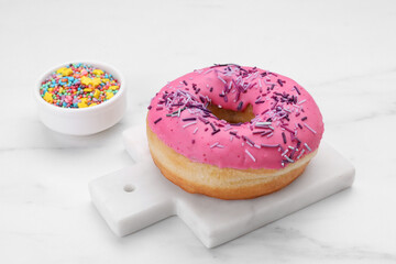 Sweet glazed donut decorated with sprinkles on white marble table. Tasty confectionery