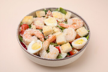 Fototapeta na wymiar Delicious Caesar salad with shrimps on beige background, closeup