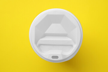 One paper cup with white lid on yellow background, top view. Coffee to go
