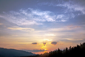 Fototapeta premium Colorful clouds in the sky at sunset against the backdrop of a mountainous forest area.
