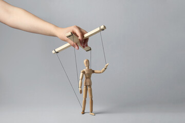 Woman pulling strings of puppet on light grey background, closeup