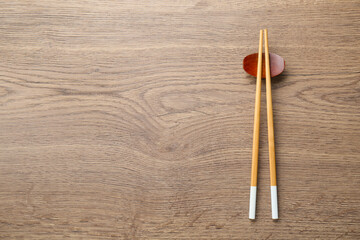 Pair of chopsticks with rest on wooden table, top view. Space for text
