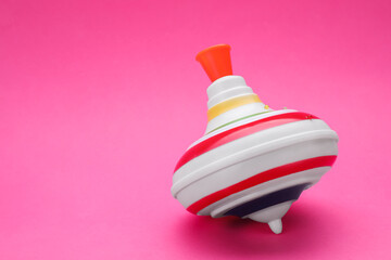 One bright spinning top on pink background, space for text. Toy whirligig