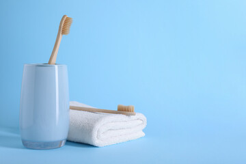 Bamboo toothbrushes and towel on light blue background, space for text