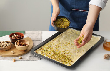 Making delicious baklava. Woman adding chopped nuts to dough at white wooden table, closeup. Space...