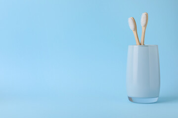 Bamboo toothbrushes in holder on light blue background, space for text