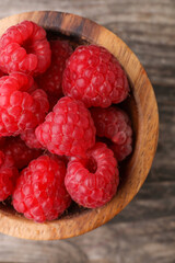 Tasty ripe raspberries in bowl on wooden table, top view