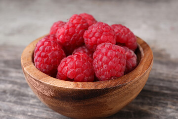 Tasty ripe raspberries in bowl on wooden table, closeup