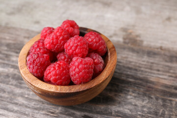 Tasty ripe raspberries in bowl on wooden table, space for text