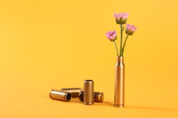 Bullet cartridge cases and beautiful chrysanthemum flowers on yellow background, space for text