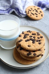 Delicious chocolate chip cookies and glass of milk on grey textured table