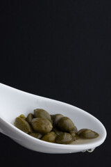 Capers in a spoon isolated on black background. Selective focus.
