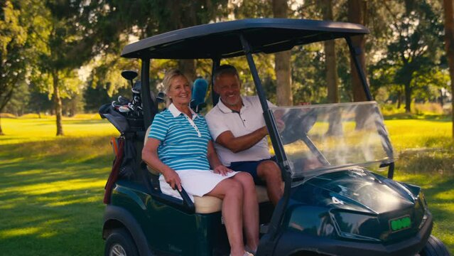 Senior retired couple ride into shot on golf buggy on course before choosing clubs - shot in slow motion