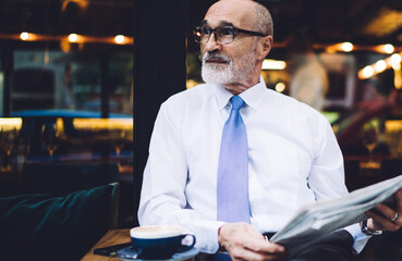 Elderly male in glasses with newspaper sitting and looking away