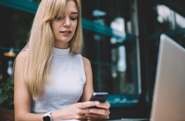 Fototapeta premium Fair-haired worker working on phone at table on porch of coffee shop