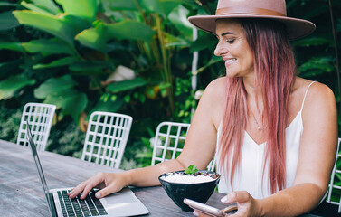 Fototapeta premium Woman typing on laptop and holding smartphone during lunchtime