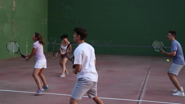 Group of sporty young people serving ball during frontenis game outdoors. Boy playing pelota on outdoor fronton.