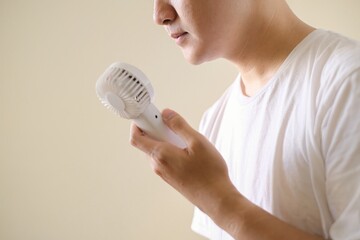 A young Asian man is using a portable fan because of hot weather