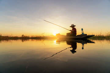Silhouette Fisherman catching the fish from wooden boat during sunset. Thailand culture.
