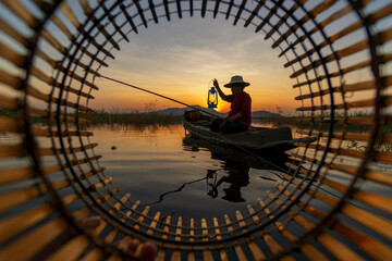 Silhouette Fisherman catching the fish from wooden boat during sunset. Thailand culture.