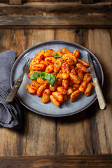 Traditional Italian potato Gnocchi with tomato sauce and fresh basil on blue plate on wooden background.
