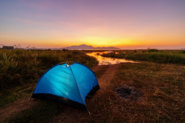 Tourist tent on camping site on the meadow next to the lake during sunset, Thailand. Beautiful sunset twilight sky
