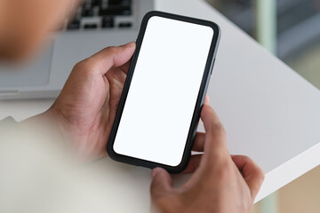 Close up view of man hands holding smart phone over working desk. Blank screen for your advertise design.