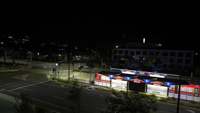 Cars and light rail trains drive passing by the bus stop at night in Canberra, Australia