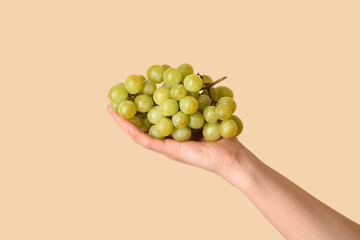Female hand holding ripe grapes on yellow background