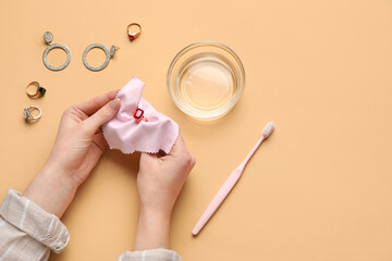 Woman polishing beautiful ring with napkin on color background, closeup