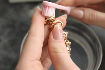 Woman cleaning beautiful bracelet with toothbrush, closeup