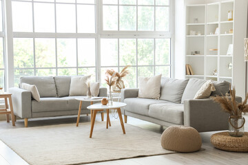 Interior of light living room with cozy grey sofas and coffee table near big window