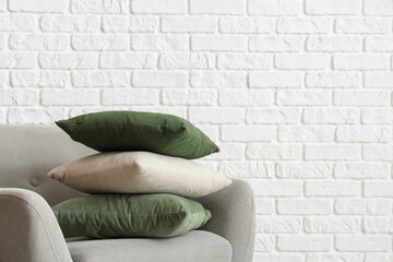 Grey armchair with cushions near white brick wall