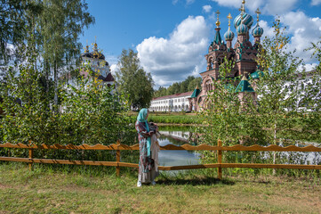 Fototapeta premium A pilgrim woman near a pond against the backdrop of the walls and temples of the Convent.