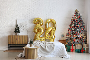 Balloons in shape of figure 2024 on comfortable bed in festive bedroom with Christmas decor
