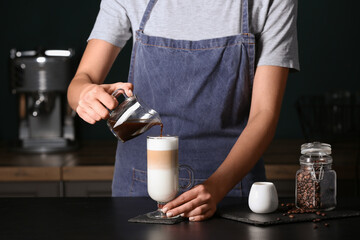 Barista pouring espresso from jug into glass with latte in cafe