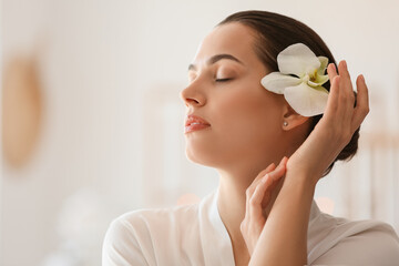 Young woman with flower relaxing in spa salon, closeup