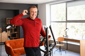 Sporty mature man in headphones training on elliptical at home