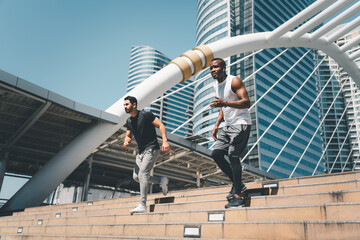 Two men working out on the stairs. Man running upstairs on city stairs.  Low angle view of young men in sport clothing running down together. Fitness, sport city, morning workout concept.