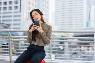 Fototapeta premium Beautiful Asian woman traveler relaxes while listening to music Young Asian tourist waits for public transportation in the city Solo travel itinerary Young female office worker resting on long holiday